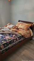 Photo of single wood sleigh bed fully assembled with floral mattress and comforters, showing polished curved headboard and footboard.