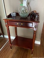 Front view of the Bombay style hall table showing drawer, brass handles, and items on top.