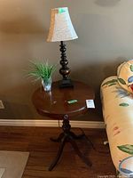 Photo of the full round wood table with lamp and plant on it, showing the claw feet and round tabletop surface.