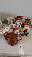 Table display of assorted ceramic pottery items including teapots, pitchers, vase, pot on stand and four small cups.