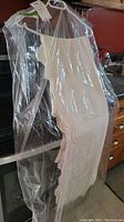 Long vintage lace tablecloth hanging on a hanger wrapped in clear plastic.
