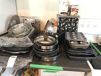 Photo showing stacked muffin tins, pie tins, cookie sheets, frying pans with lids, metal food racks on countertop