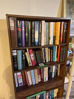 Photo showing the full bookshelf with three shelves filled with books, a mix of hardcover novels on top, and paperbacks below