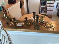 Photo showing three brass bells, two single candlestick holders, one double candlestick holder, small brass pitcher, and a flat key holder.