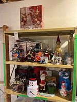 Overview of the Christmas decor items displayed on shelving including candy dish, Norman Rockwell village houses, figurines like snowmen, nutcracker soldiers, Santa figure, and candle holders.