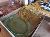 Assorted coloured glass dishes including pink depression glass bowls and plates, yellow pressed glass decorative plate, and green glass plate
