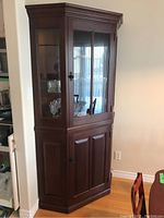 Front view of the dark wood corner display cabinet with glass top doors showing glassware inside and solid wood bottom doors.