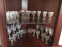 Shelf with various crystal stemware glasses including wine and cocktail glasses arranged in sets.