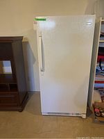 Front view of white Frigidaire upright freezer with door closed and handle on left side