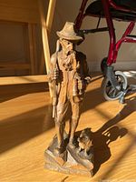 Full front view of the Josef Buhner wood carving showing the hunter holding a rifle with his dog at his feet on the carved base.