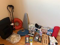 Wide view of most items on the floor including two walking canes, orange seat cushion, blue balance disc, wooden foot massager, red bolster cushion, gloves, and boxed monitors.