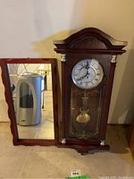 Wood pendulum wall clock next to wooden framed mirror showing overall size and look of each item