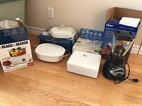 Wide shot showing all items: Oster blender, boxed Black & Decker mixer kit and steamer, two Corning Ware casseroles.