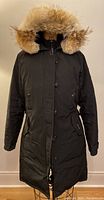 Front view of black Kensington parka on mannequin with hood up and fur trim.