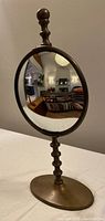 Front view of oval convex mirror on turned spindle stand with antique bronze finish showing interior reflection.