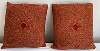 Pair of wool patterned decorative pillows with orange and red intricate design shown from front.