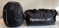 Photo showing both black Reebok duffel bag and MEC backpack side-by-side on a light surface.