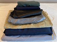 Stacked pieces of various fabrics in shades of green, navy, black, grey and patterned gold