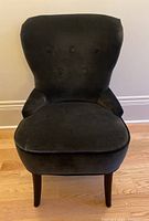 Front view showing the curved button tufted backrest and padded seat of the grey upholstered chair.