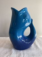 Front angle showing the fish mouth spout and curved fish tail handle of the glossy blue gurgle pot.