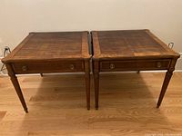 Full front view of both square wood side tables showing single drawers, turned legs and brass drawer pulls