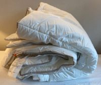 Folded white duvet with grey striped edge visible, showing overall condition and size.