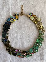Full view of multicoloured stone necklace laid flat showing variety of shaped and coloured stones set in gold metal.
