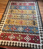 Full view of the Kilim rug showing the colorful horizontal bands, geometric patterns, and border design.