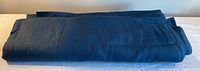 Folded bolt of dark blue linen fabric on neutral surface