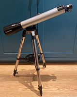 Full view of the Meade refractor telescope mounted on the adjustable tripod with black feet and central tray, showing the full length and structure.