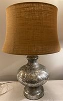 Full view of the lamp showing the mercury glass base and burlap lampshade.