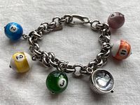 Close-up of the billiard ball charms on the silver chain bracelet, including the 8 ball watch face charm.