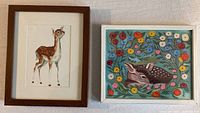 Pair of framed deer prints, left brown wood frame with watercolor standing fawn, right white frame with colorful fawn and flowers print.