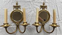 Two vintage brass wall sconces with mirrors and two candle holders each, shown side by side on a fabric background.