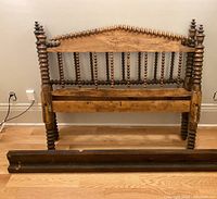 Front view of wood spool headboard with spindles and turned posts, showing wear and some damage at joints. Side rails laid on floor in front.