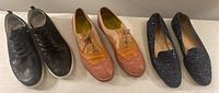Three pairs of women's shoes displayed side by side on a table: black Geox lace-up brogues, blush/orange/pink leather brogues, and navy glitter slip-on shoes.