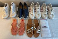 All 7 pairs of women's shoes shown in a single image, including Adidas Boost sneakers, Everlane slip-ons, Gola sneakers, Dolce Vita sandals, Cole Haan sandals, and Gekks liners laid out.