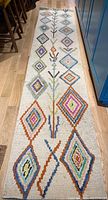Full view of colorful runner rug characterized by multi-colored diamond shapes on a cream background and elongated botanical motifs.