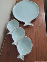Two light blue ceramic fish-shaped serving dishes placed on wooden surface. One large single fish dish; one dish divided into three smaller fish shapes, all with brown edges.
