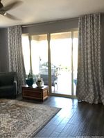 Curtain panels hanging over large patio sliding glass doors in living room setting. Curtains are gray with geometric pattern and silver grommets.