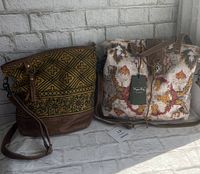 Two Myra bags side by side on surface against white brick wall. One bag has brown geometric and floral canvas with leather base and strap. Other bag shows colorful woven canvas with leather handles and silver clasp, tag attached.