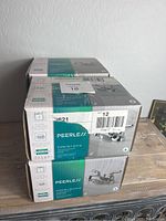 Four boxed Peerless P299618LF-ECO-W bathroom faucets stacked on a table showing the brand and model