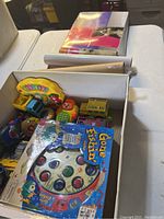 Box containing Gone Fishin' fishing game, toy school bus, colorful educational toys and puzzle pieces.