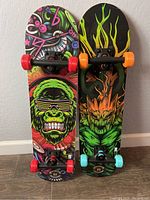 Photo showing two new skateboards side by side with colorful graphic decks and variously colored wheels.