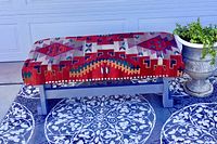 Front angle view of the wool serape upholstered bench with southwestern geometric patterns and grey wooden base.