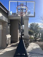 Full front view of the basketball hoop standing outdoors in front of a house showing the base, pole, clear backboard with Spalding branding, red rim and net.