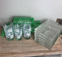 Set of 6 snowflake patterned tumblers and 6 clear Altas glass plates displayed on wooden surface with green textured glass items behind