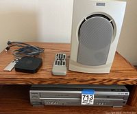 Photo of Apple TV unit, white remote, cords, white speaker, and Sanyo DVD/VCR unit with label