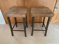 Front view of two brown upholstered bar stools with black metal frames showing the overall height and seat size
