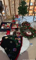 Wide shot of Christmas wreaths, artificial tree, ornaments in boxes, tree skirts, and other decorations on floor and table